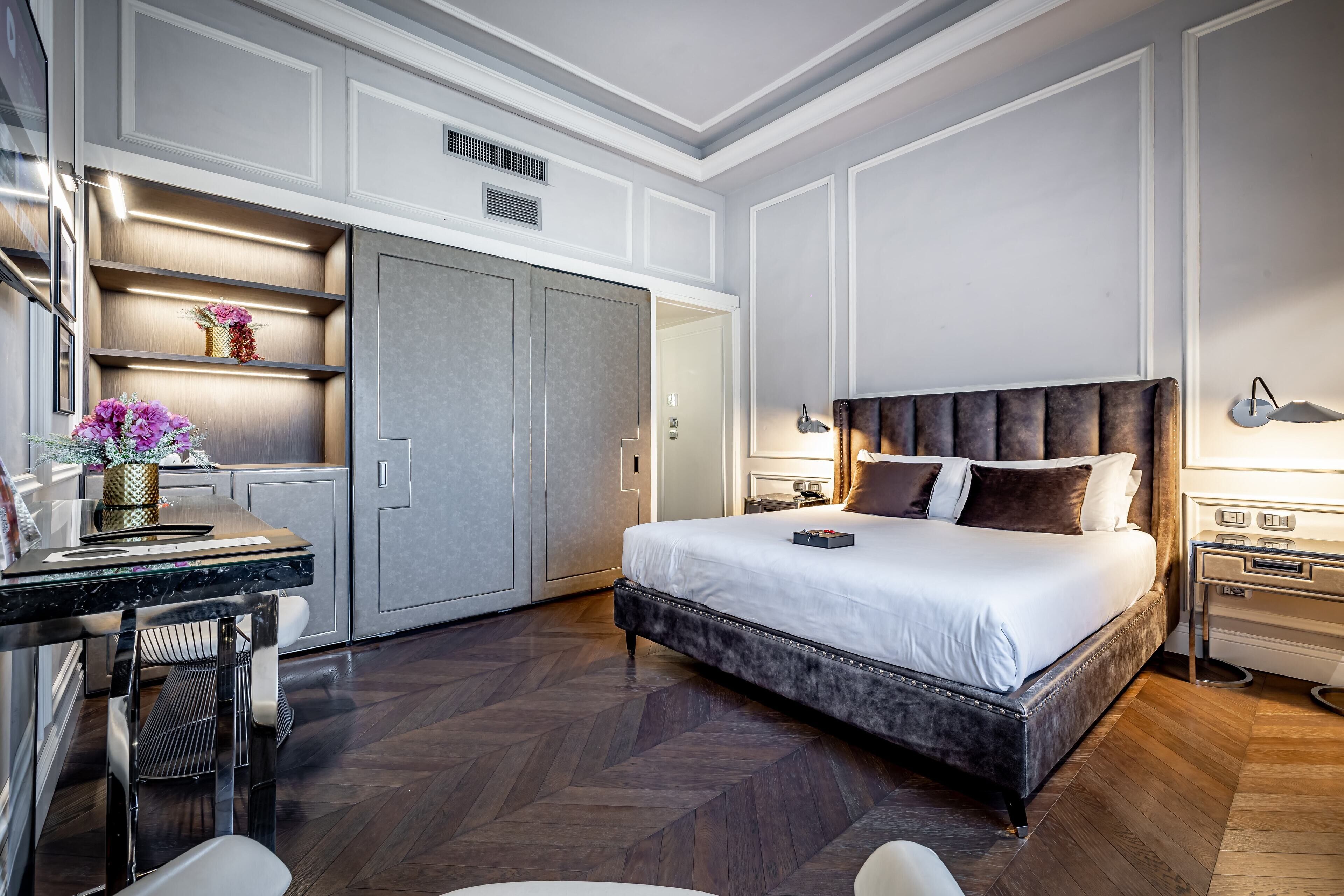 Una habitación de hotel moderna con una cama grande, un escritorio con silla, un armario y una mesita de noche con lámpara.