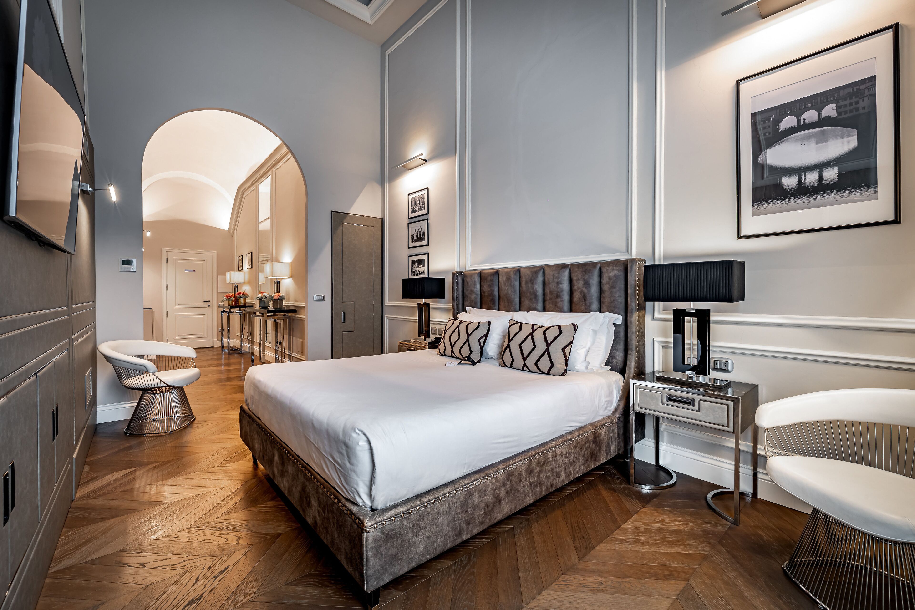 A modern hotel room with a large bed, a vanity with a mirror, a desk, and a chair.
