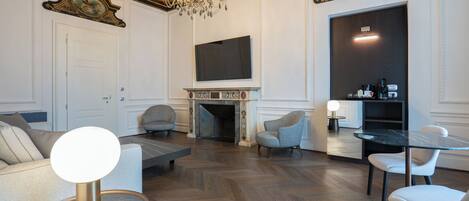 A spacious living room with a fireplace, a television mounted above it, and a chandelier.