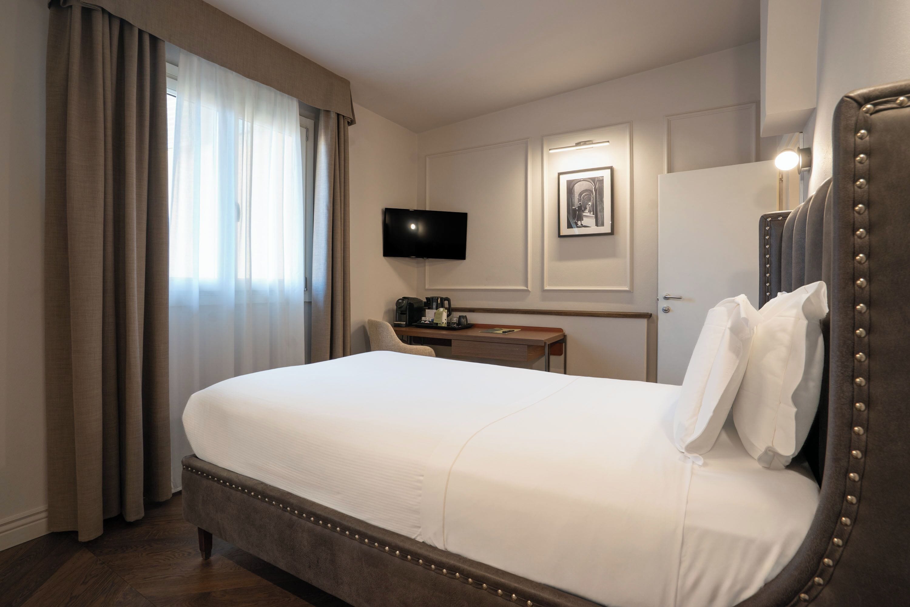 A hotel room with a large bed, a desk with a flat-screen TV, and a framed picture on the wall.