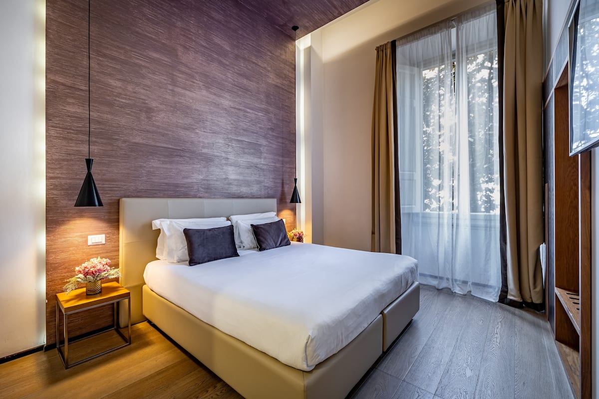A modern hotel room with a large bed, a wooden accent wall, and a view of the outdoors.