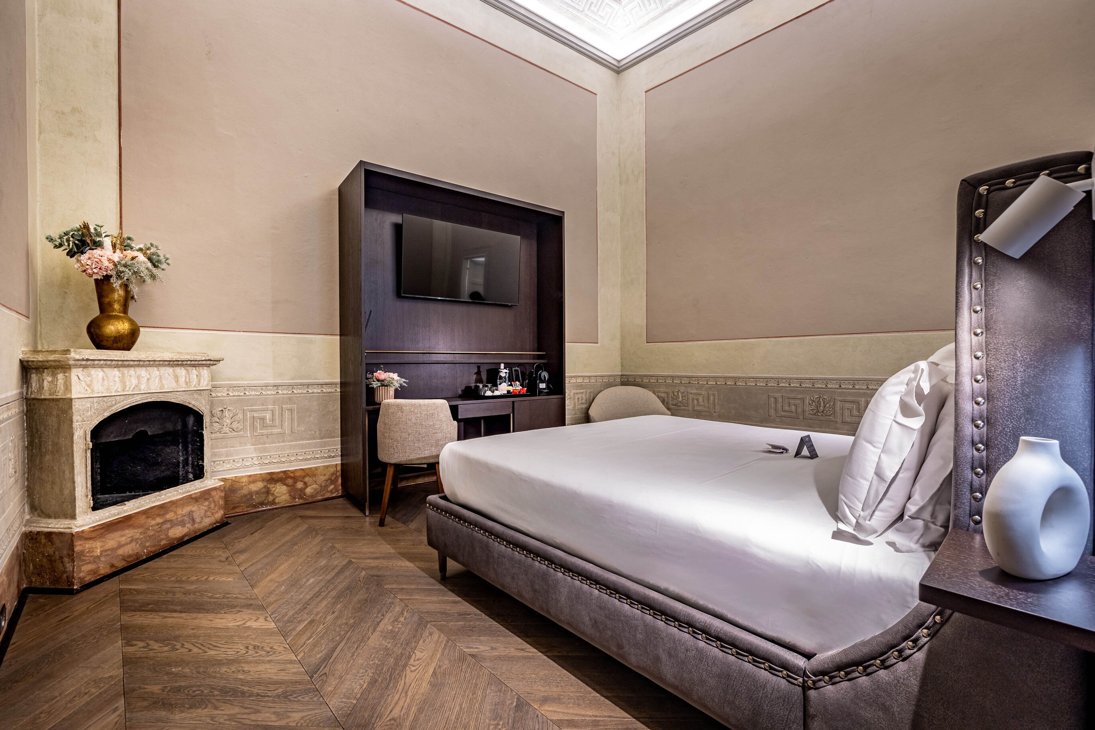 Une chambre d’hôtel avec un grand lit, une cheminée, un bureau avec une chaise et un téléviseur.