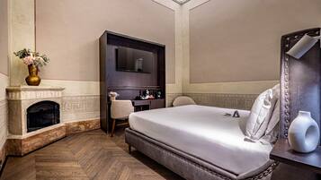 Quarto de hotel com uma cama grande, lareira, escrivaninha com cadeira e televisão.