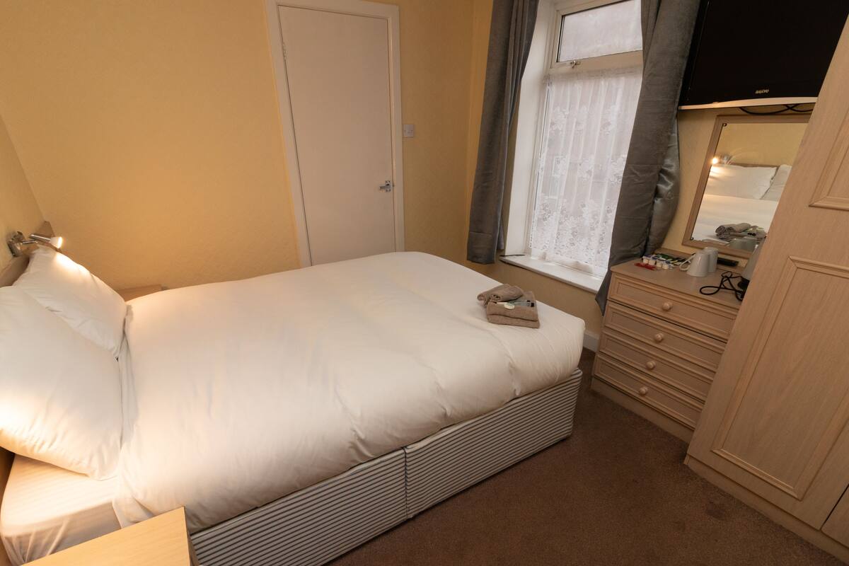 Un dormitorio con cama, mesita de noche, cómoda y ventana con cortinas.