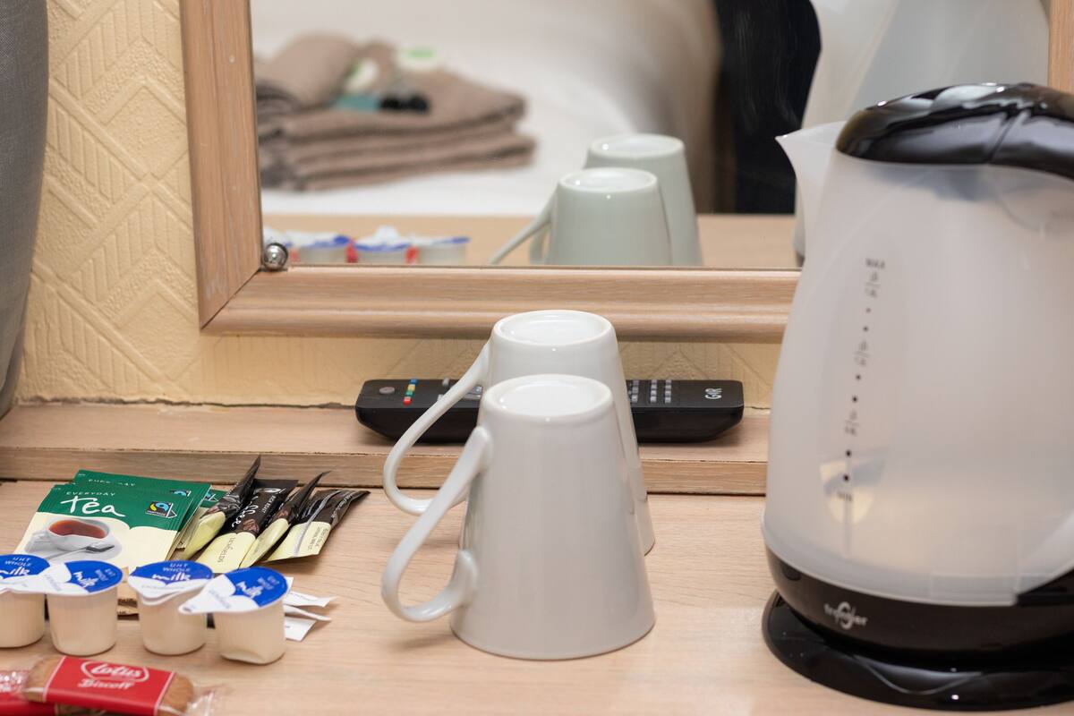 Habitación de hotel con una mesa de madera, una cafetera, dos tazas blancas, un control remoto y sobres de té y café.