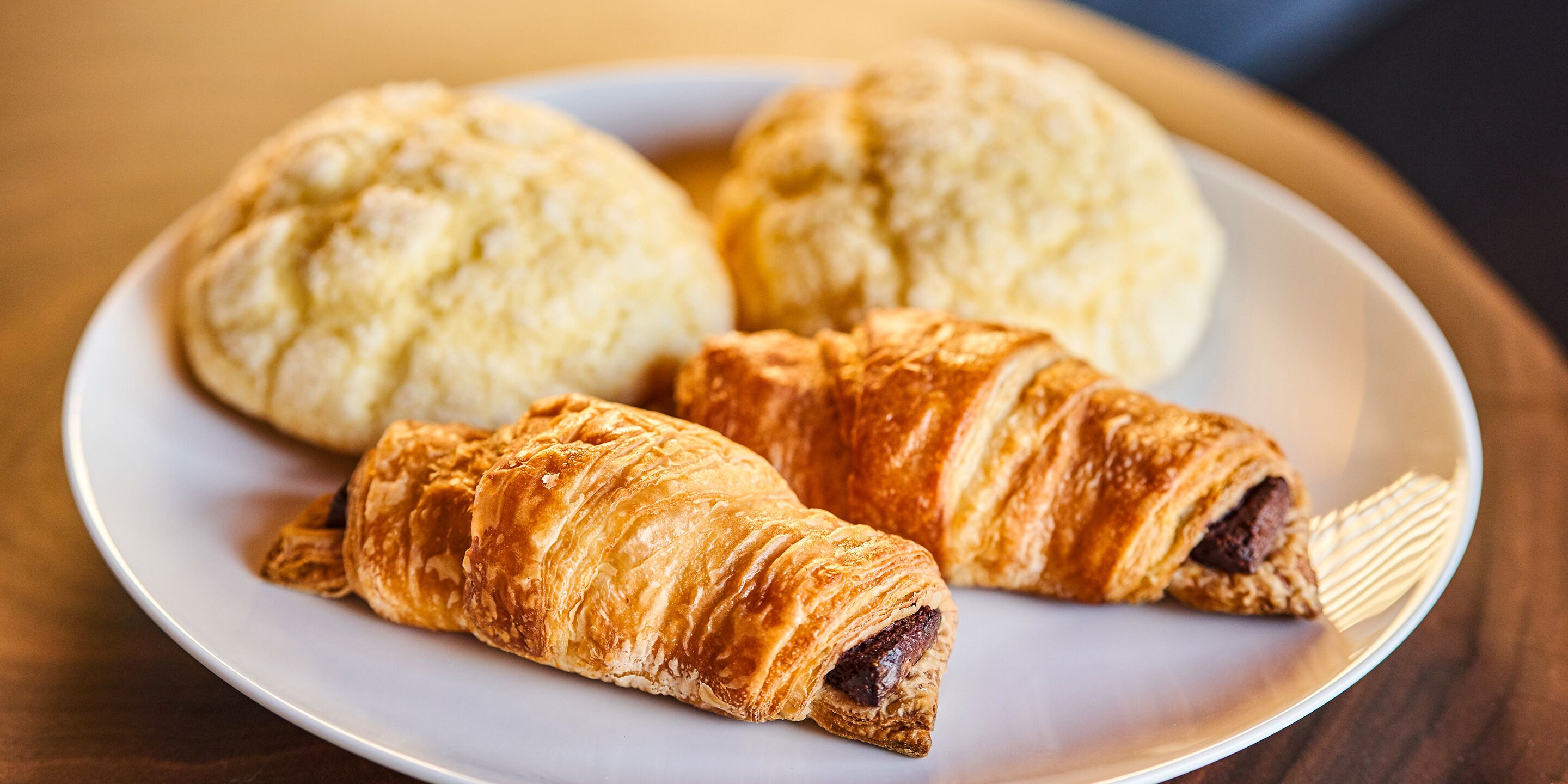 A plate with three pastries: two croissants and one round bread.