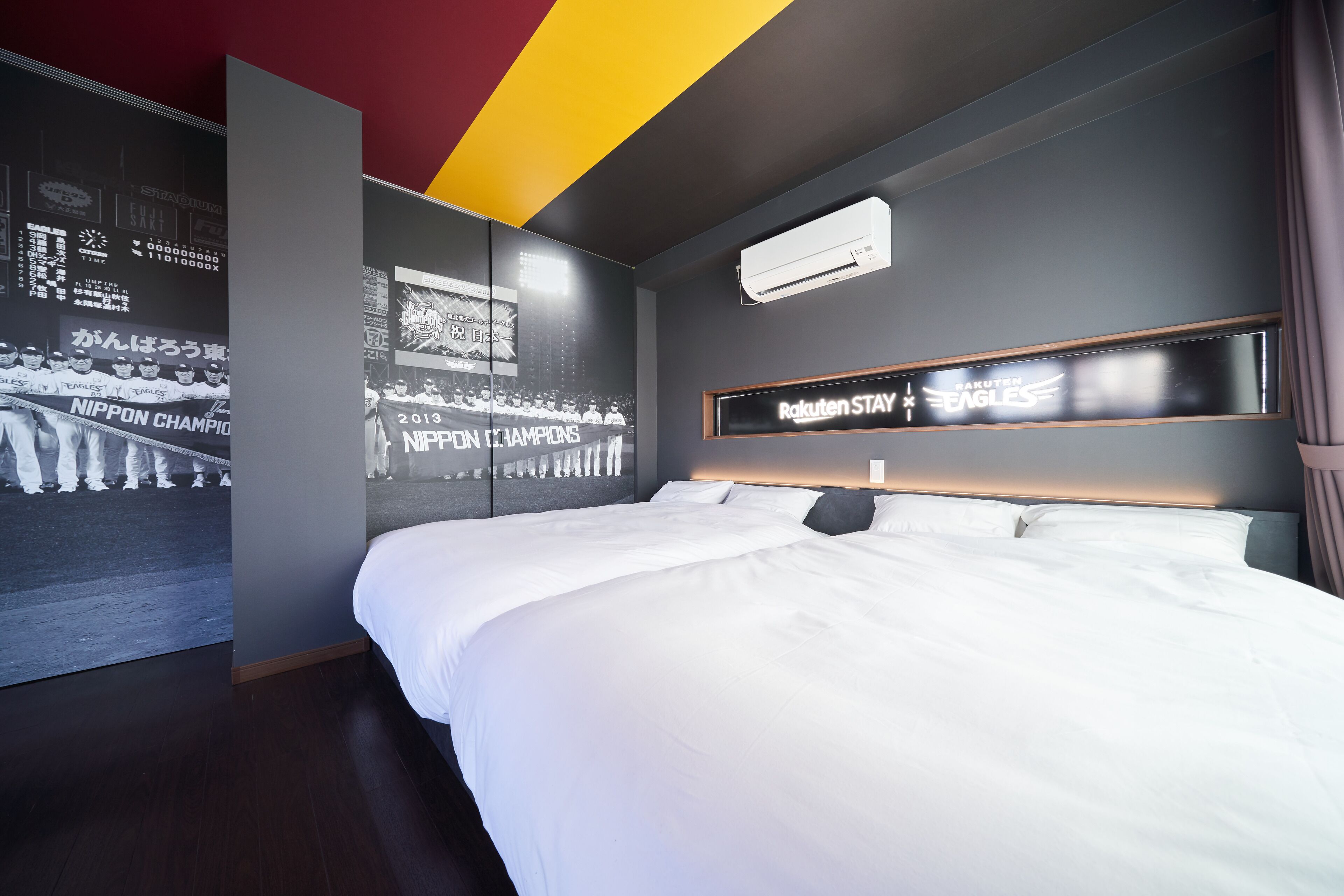Quarto de hotel com uma cama grande, ar-condicionado fixado na parede e uma placa com a inscrição 'Rakuten Eagles'.