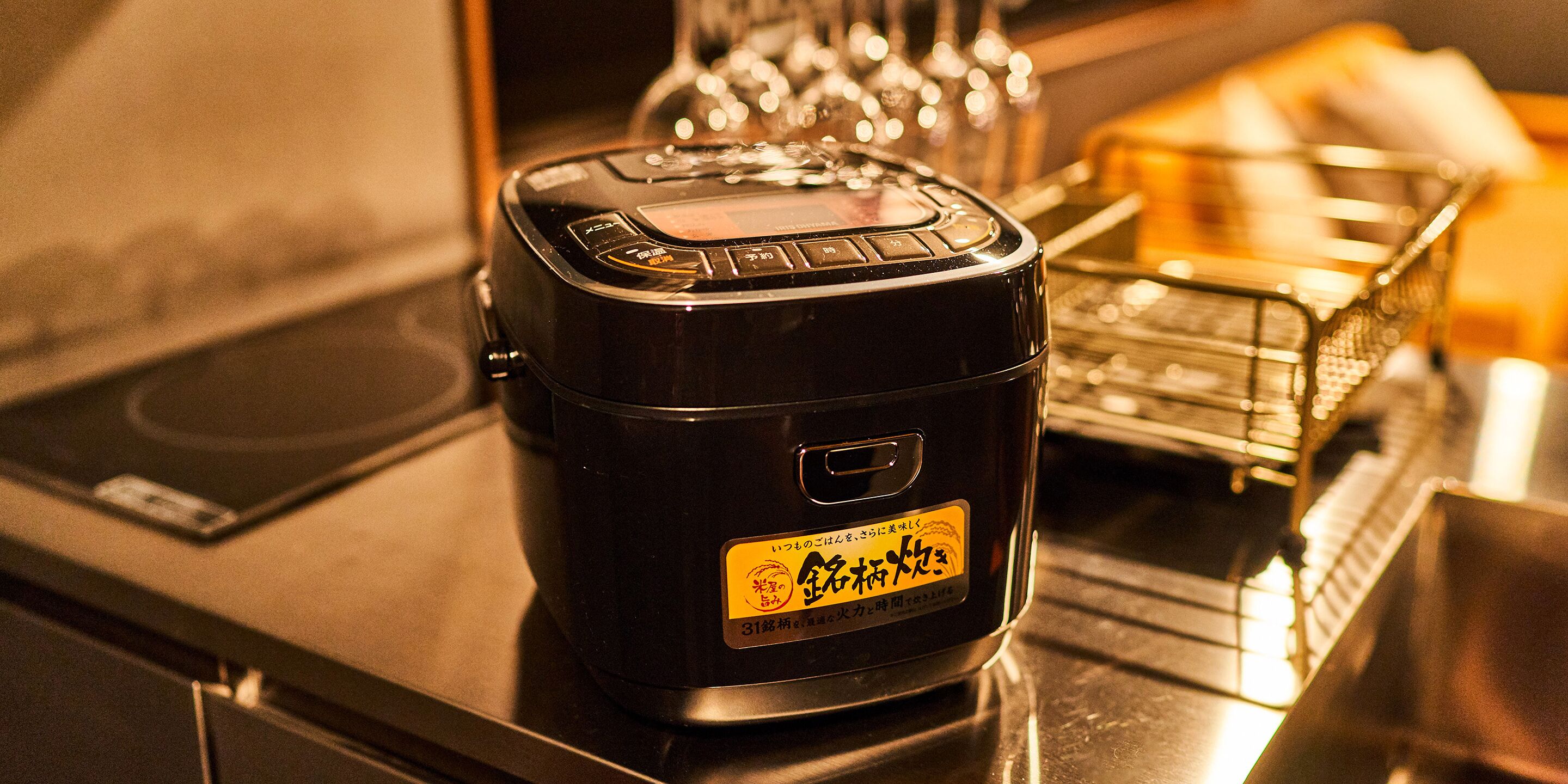 A black rice cooker with a yellow label on a kitchen counter.
