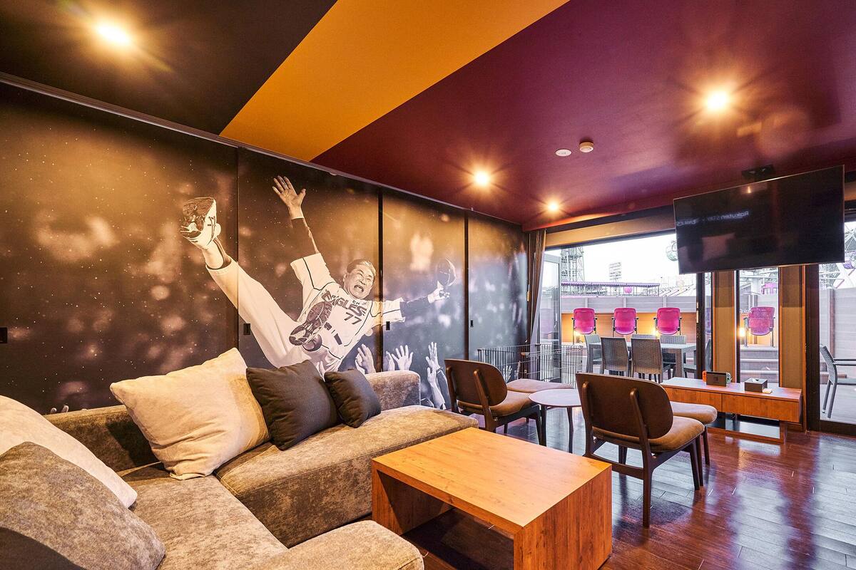 A modern interior with a sofa, wooden table, and chairs. There is a large TV on the wall and a mural depicting a baseball player.