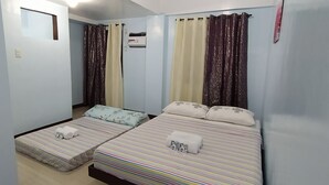 Habitación con dos camas, cada una con ropa de cama y almohadas a rayas, una ventana pequeña y un equipo de aire acondicionado en la pared.