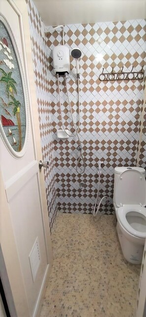 A bathroom with a patterned tile wall, a shower, a toilet, and a mirror with a decorative frame. - JB Valdres Apartment (Parañaque)