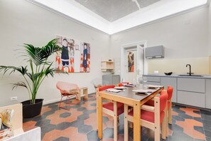 A modern kitchen with a dining area, featuring a large potted plant, a dining table with red chairs, and a kitchen counter with a sink and cabinets.