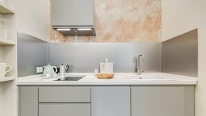 Eine moderne Küche mit grauen Schränken, einer weißen Arbeitsplatte, einer Edelstahlspüle, einem Wasserkocher und einer Insel mit Marmorplatte.