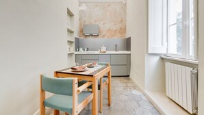 Eine kompakte Küche mit Einbauofen, einem kleinen Esstisch mit Stühlen und einem Fenster, das natürliches Licht hereinlässt.
