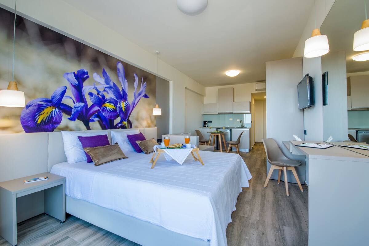 Ett modernt hotellrum med en stor säng, en matplats och ett kök i bakgrunden.