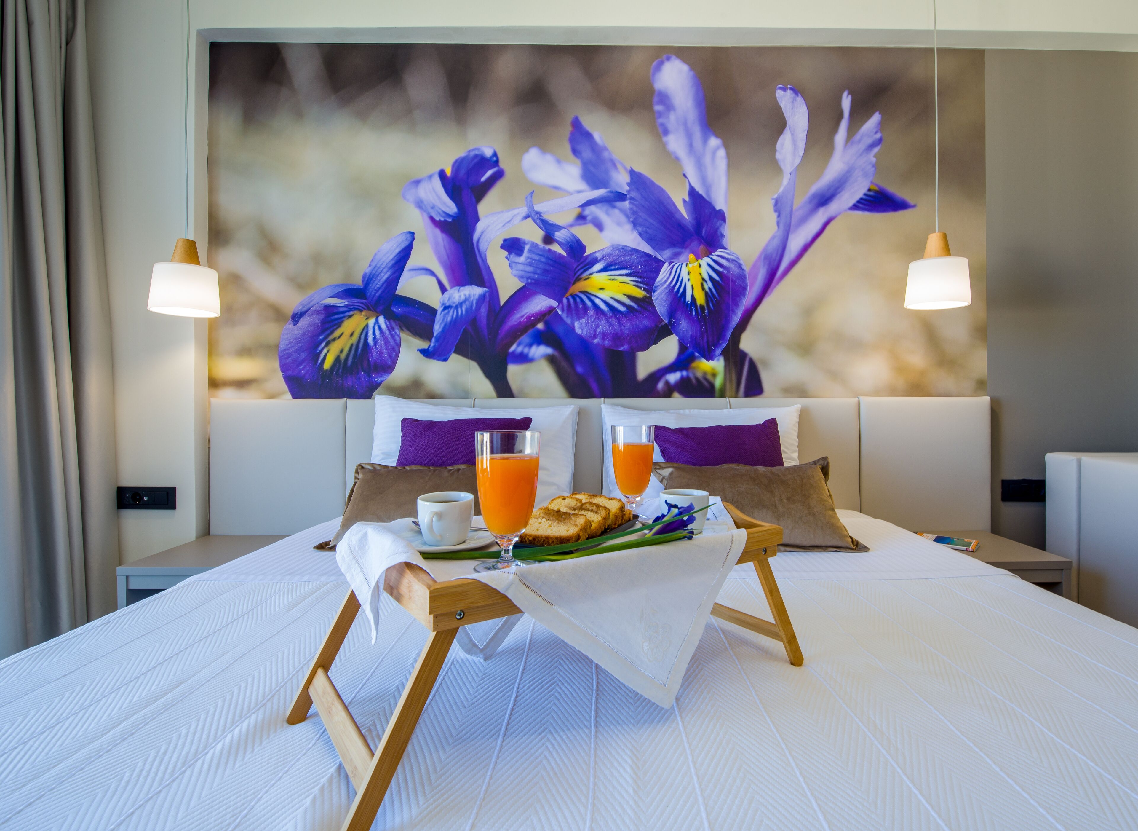 A neatly made bed with a breakfast tray, two glasses of orange juice, and a cup of coffee.