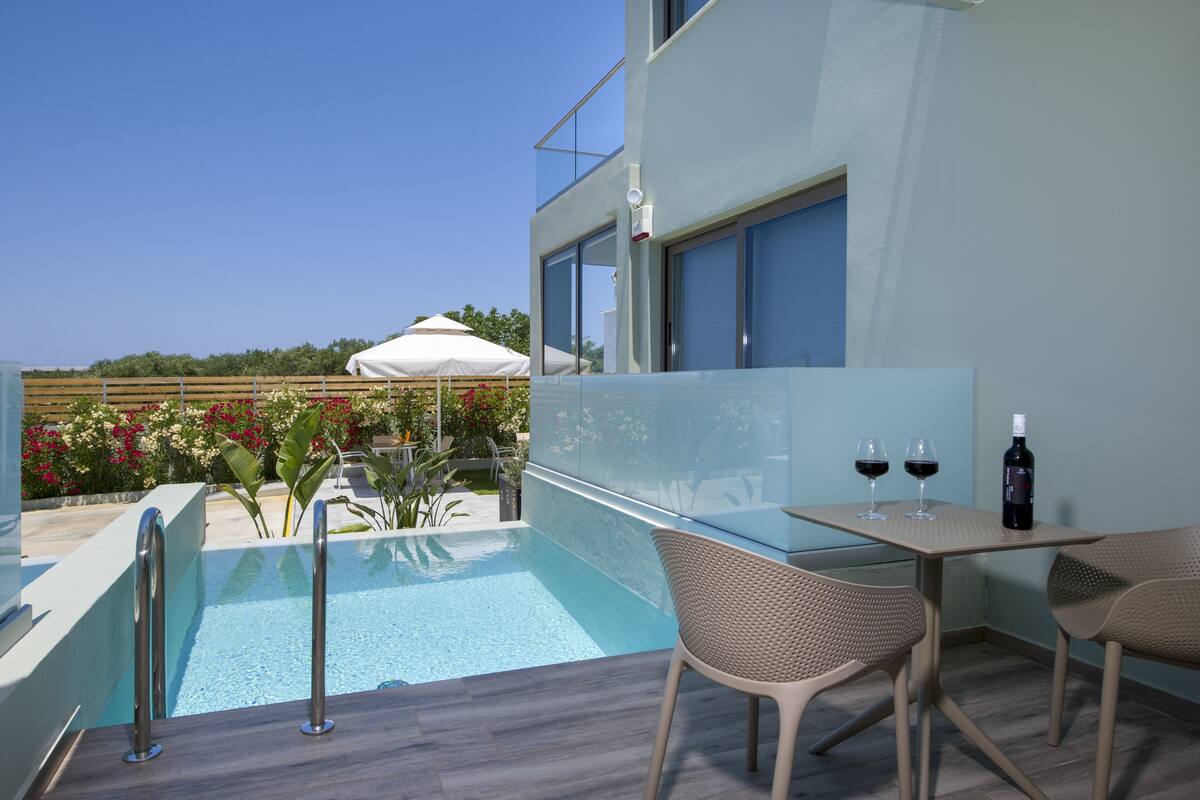 Ett modernt utomhusområde med pool, ett glasbord och stolar, en bar vid poolkanten och utsikt över havet.