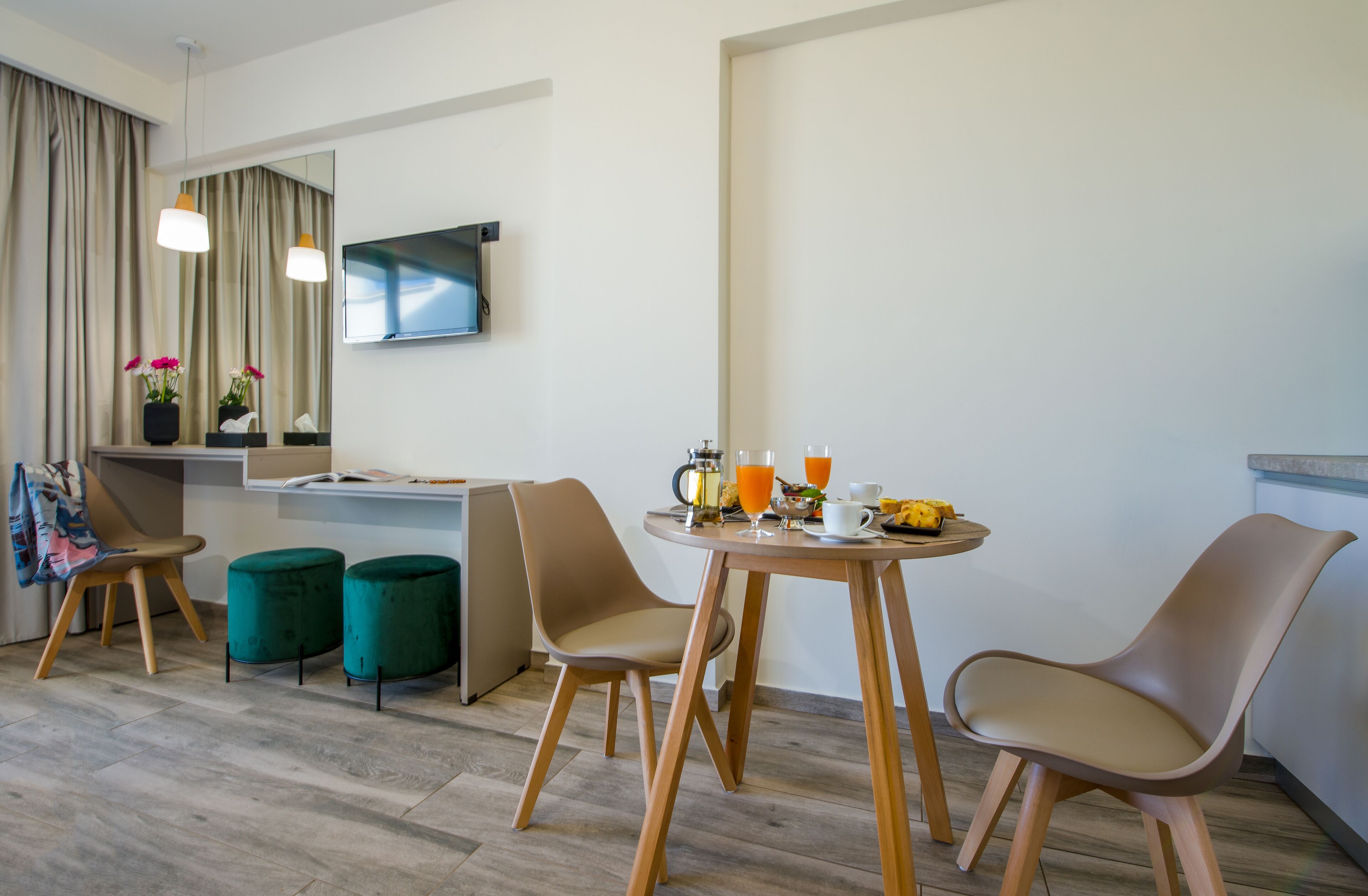A modern hotel room with a dining area, a flat-screen TV, and a small kitchen counter.
