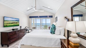 A spacious bedroom with a large bed, a ceiling fan, a TV on the wall, and a balcony with a view. - Ocean Front Luxury Condo Panoramic Views of the Caribbean Sea  (George Town)