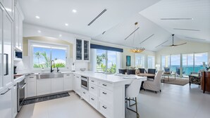 A modern kitchen with white cabinetry, a large island, and a dining area with a view of the ocean. - Ocean Front Luxury Condo Panoramic Views of the Caribbean Sea  (George Town)