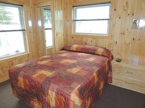 Une pièce en bois avec un lit, deux fenêtres et une armoire en bois.