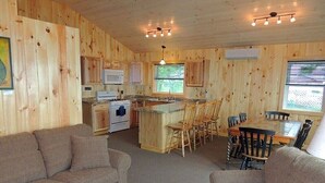 Un intérieur de chalet chaleureux comprenant un salon, un coin repas, une cuisine et une grande fenêtre.