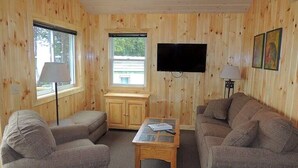 Une pièce chaleureuse avec des murs en bois, un téléviseur à écran plat fixé au mur, une fenêtre donnant sur un beau paysage et deux canapés.