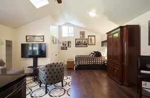 A spacious living room with a flat-screen TV, a patterned armchair, a sofa, and a large wooden cabinet.