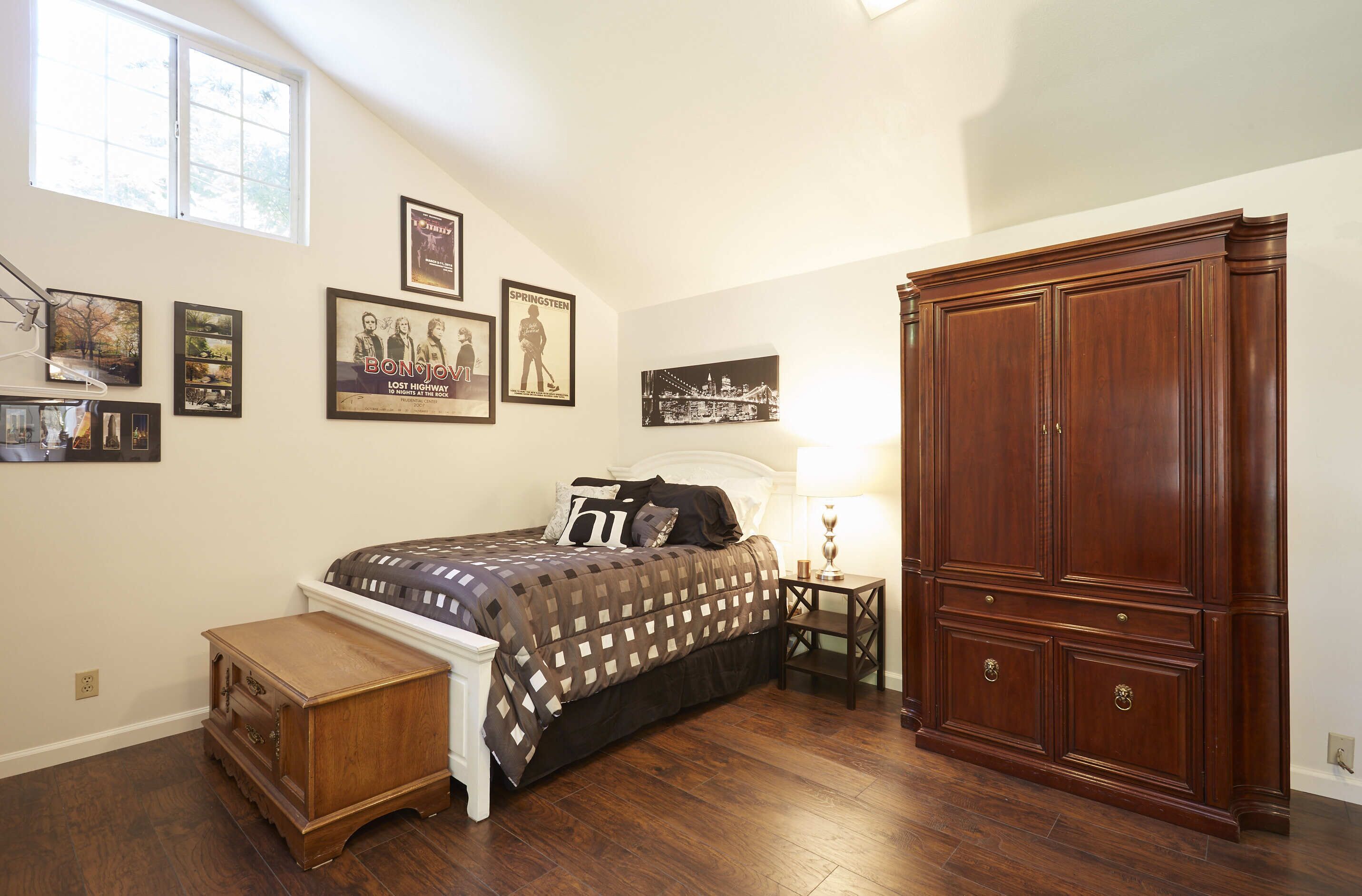 A bedroom with a bed, nightstand, dresser, and wall art.