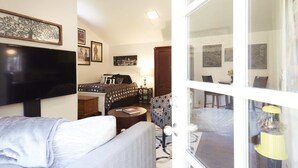 A hotel room with a bed, a TV, a sofa, a patterned armchair, and a window with a view of the street. - Private Willow Glen Studio Guesthouse (San Jose)