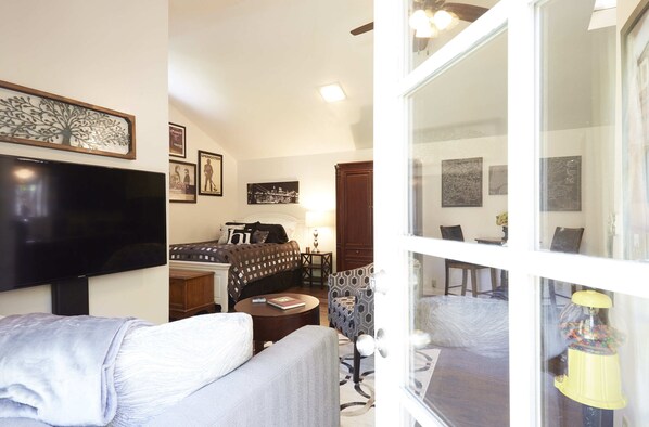 A hotel room with a bed, a TV, a sofa, a patterned armchair, and a window with a view of the street.