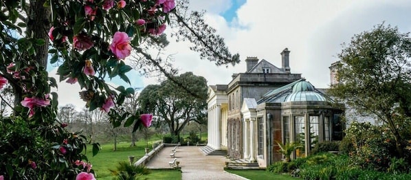 A classical building with a glass dome and columns, surrounded by a well-maintained garden and a pathway leading to the entrance.