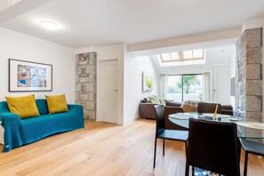 A modern living room with a blue sofa, a dining table with chairs, and a stone accent wall. - Bright Flat with Estuary Views & Parking, Falmouth (Falmouth)