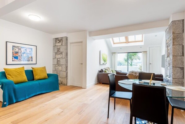 A modern living room with a blue sofa, a dining table with chairs, and a stone accent wall. - Bright Flat with Estuary Views & Parking, Falmouth (Falmouth)