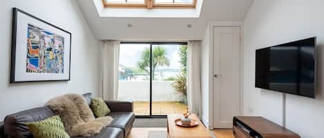 A modern living room with a sofa, a coffee table, a flat-screen TV, and a skylight.