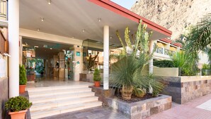 A hotel entrance with a covered patio, steps leading to the entrance, and potted plants.