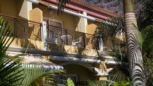 A building with a yellow facade, a red-tiled roof, and a balcony with metal railings.