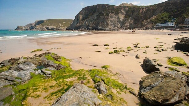 Une plage avec des zones rocheuses et un bâtiment en arrière-plan.