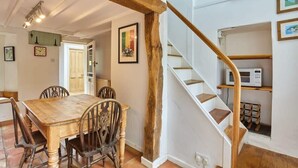 Un coin repas avec une table et des chaises en bois, un escalier avec des rampes en bois et un mur blanc orné d’un tableau encadré.