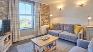 A cozy living room with a stone wall, a grey sofa with yellow cushions, a wooden coffee table, and a television on a wooden stand.