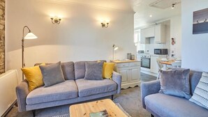 A modern living room with a grey sofa, yellow and grey cushions, a wooden coffee table, and a kitchen in the background.