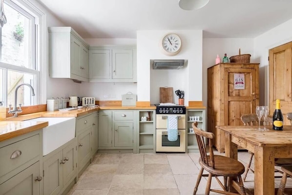 Een keuken met lichtgroene kastjes, een houten tafel met stoelen, een klok en een houten kastje met een bord.