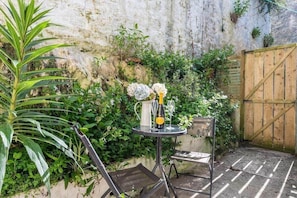 Een terras met een tafel gedekt voor twee personen, omgeven door groen en een rustieke muur.