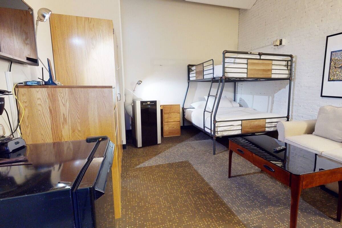 Una habitación compacta con literas, un sofá, una mesita y un escritorio con lámpara.