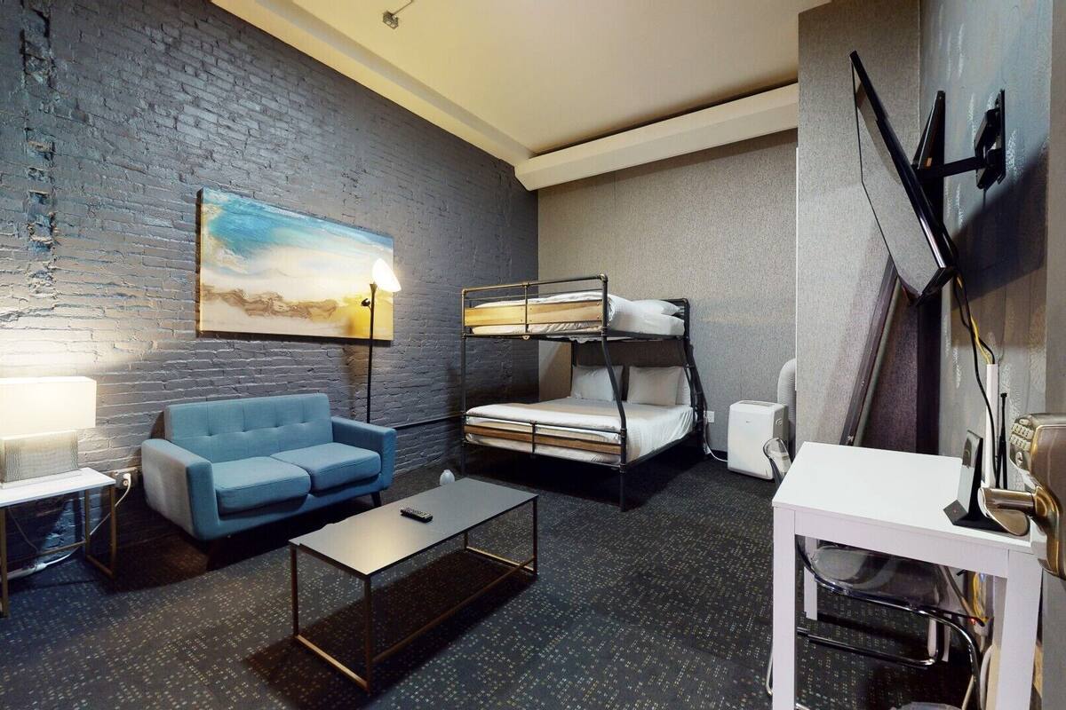 Una habitación de hotel moderna con sofá azul, literas, una mesa de centro y un cuadro en la pared.