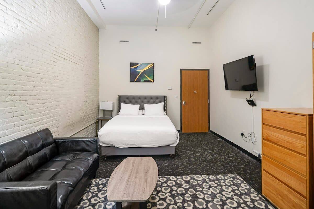 Una habitación de hotel con una cama, un televisor, un aparador de madera, un sofá de cuero y una alfombra estampada.