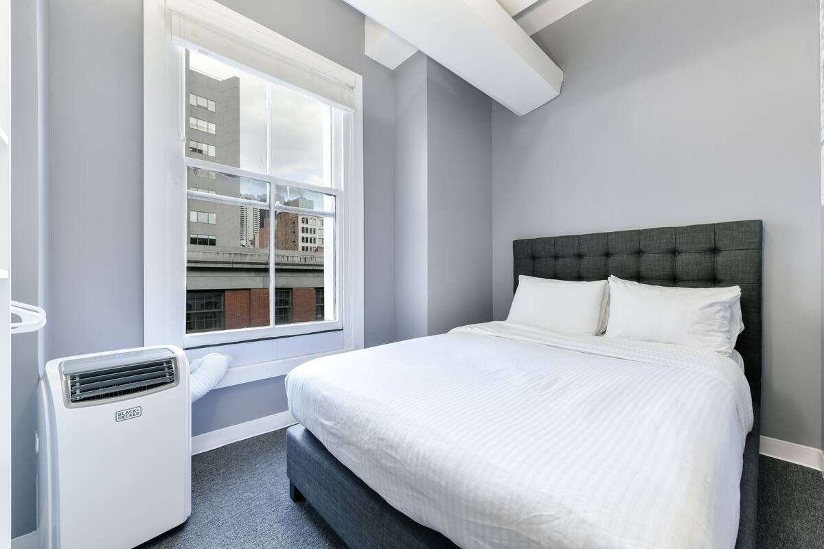 Un dormitorio con cama, ventana y aire acondicionado instalado en la pared.