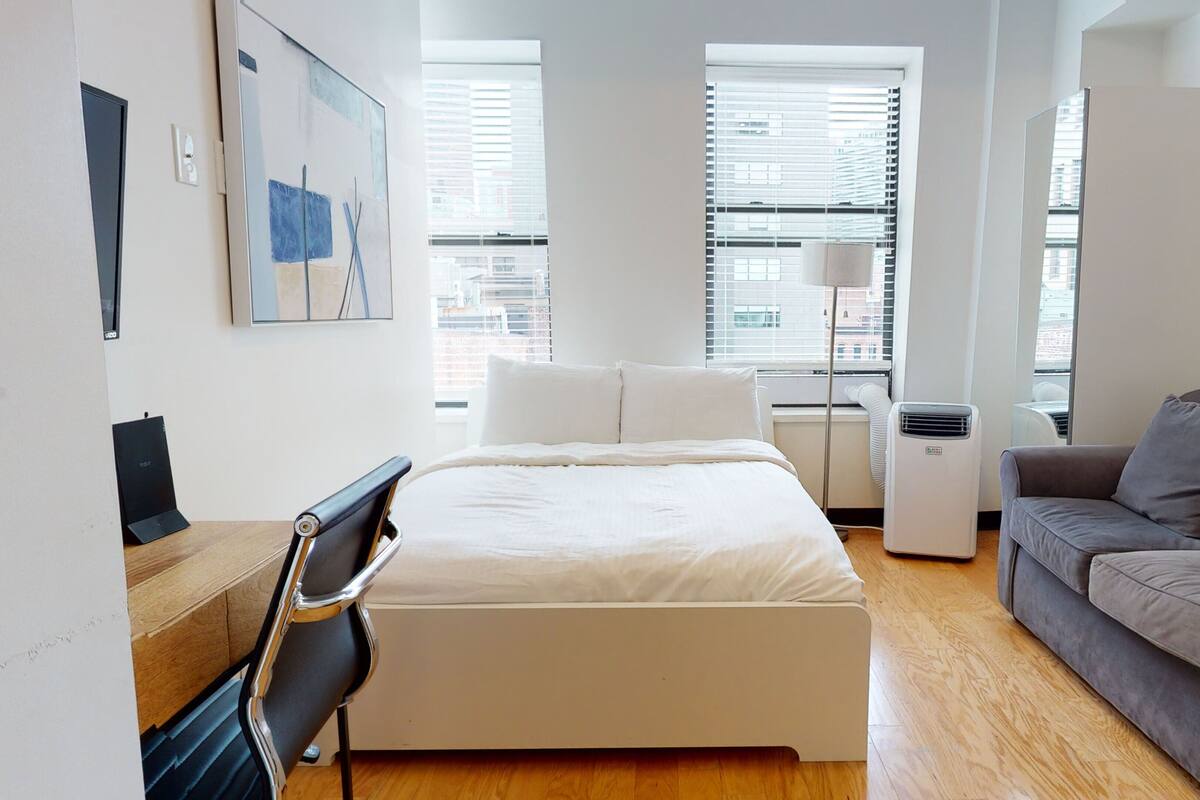 Un dormitorio moderno con una cama, un escritorio, una silla, un sofá y un ventanal grande.