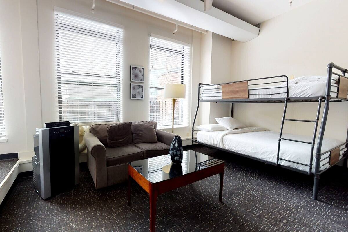 Una habitación de hotel compacta con literas, un sofá, una mesita de centro y un calentador.