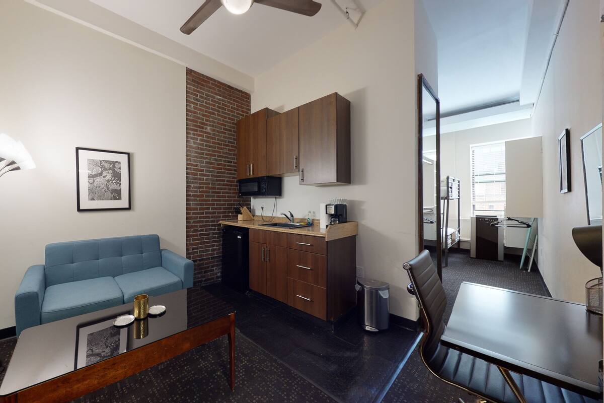 Un espacio habitable compacto con kitchenette, un sofá azul, una mesa de comedor y una lámpara de pie.